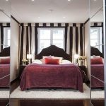 Lit élégant près de la fenêtre dans une chambre avec armoires de toilette
