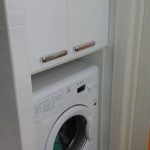 Niche dans la salle de bain avec une machine à laver et une armoire au dessus