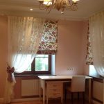 Persianas romanas florales y tul blanco para una habitación con muebles claros.