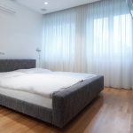 Lit gris dans la chambre à coucher avec des rideaux blancs