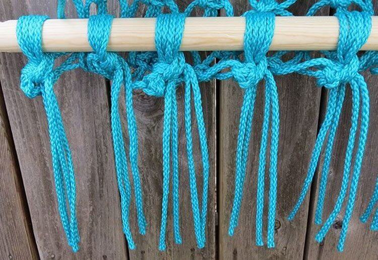 Weaving knots of turquoise rope on a wooden stick